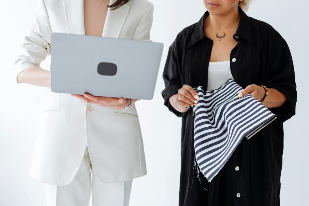 Two adults engaging in a textile design meeting, using a laptop and fabric samples.